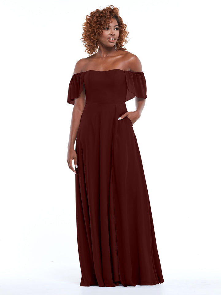 A woman models the Avery Austin 80168 dress in merlot, featuring an off-the-shoulder chiffon A-line silhouette with short sleeves and a flowing, floor-length skirt, set against a white background.