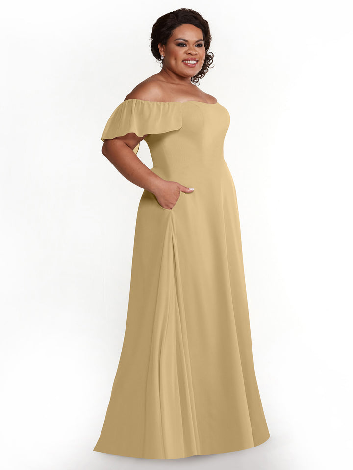A woman smiles against a white background, wearing the Avery Austin 80168—a champagne chiffon, off-the-shoulder, floor-length A-line dress with short ruffled sleeves and pockets.