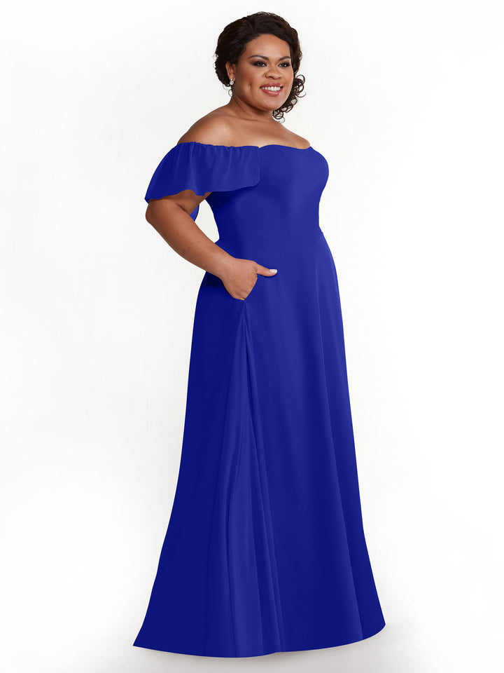 A woman smiles in the Avery Austin 80168, a cobalt chiffon off-the-shoulder A-line floor-length dress with pockets and short sleeves, standing against a plain white background.