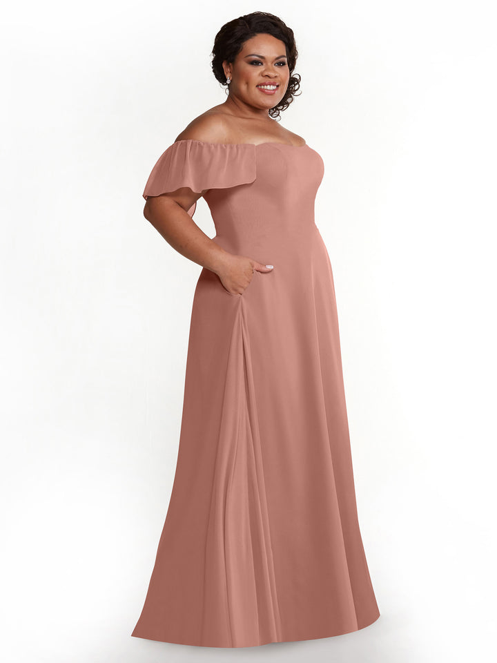 A woman smiles against a white background, modeling the Avery Austin 80168: a dusty rose chiffon off-the-shoulder A-line dress with flutter sleeves and pockets.