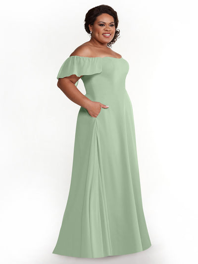 A woman smiles in Avery Austin’s 80168, a light sage green chiffon A-line dress with pockets and short ruffled sleeves, standing against a plain white background.