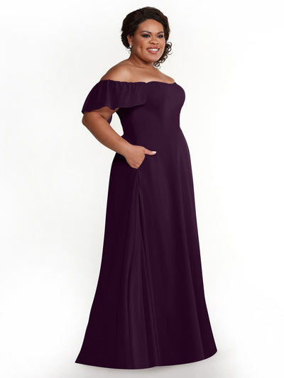 A woman models Avery Austin’s 80168: a dark purple, chiffon off-the-shoulder A-line dress with short ruffled sleeves and pockets, smiling against a plain white background.