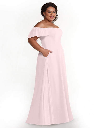 A woman smiles against a white background wearing Avery Austin’s 80168: a light pink, chiffon, off-the-shoulder A-Line dress with short ruffled sleeves and pockets.
