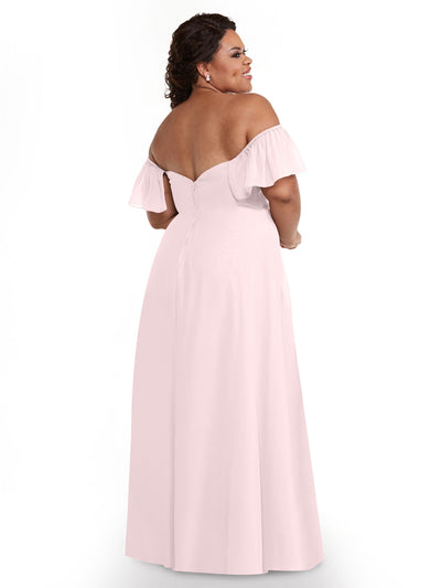 A woman in Avery Austin’s 80168 dress—light pink chiffon, off-the-shoulder A-line with ruffled short sleeves and a fitted bodice—stands facing away, looking over her shoulder and smiling against a plain white background.