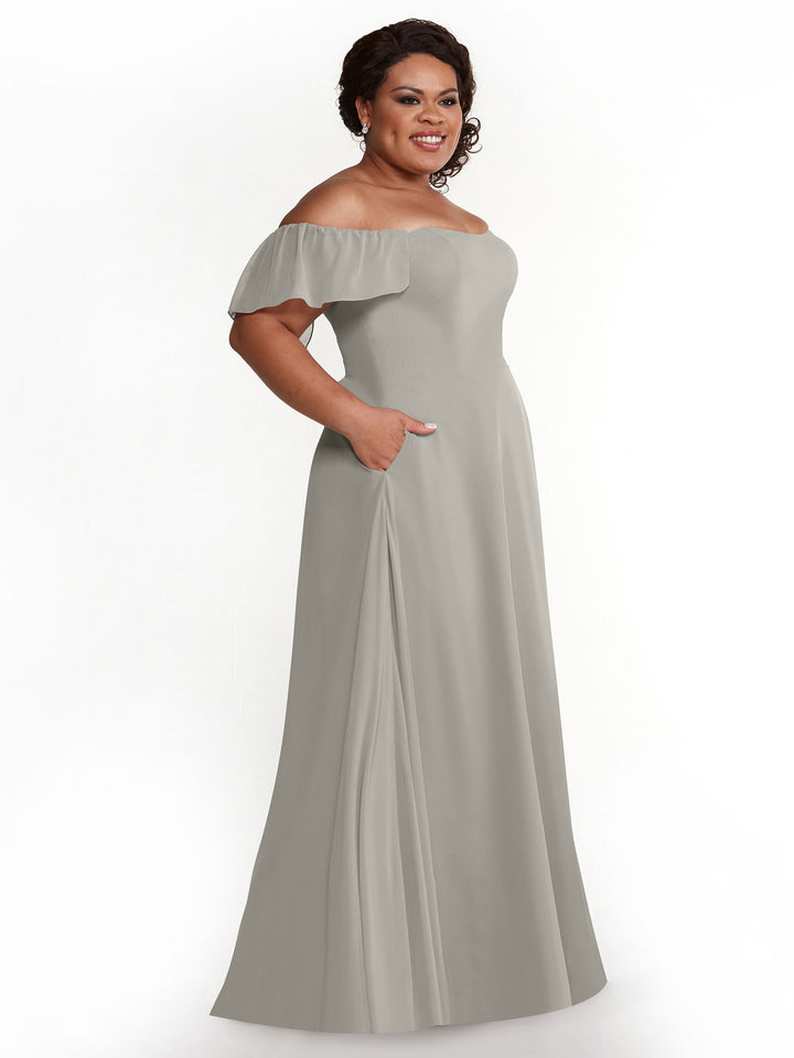 A woman smiles against a white background, wearing the Avery Austin 80168 light gray chiffon off-the-shoulder A-line dress with short ruffled sleeves and side pockets.