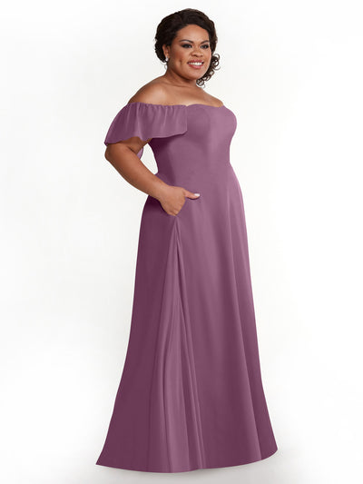 A woman wearing the Avery Austin 80168 chiffon off-the-shoulder, floor-length mauve-purple A-line dress with pockets stands smiling, her hands tucked in her pockets against a plain white background.