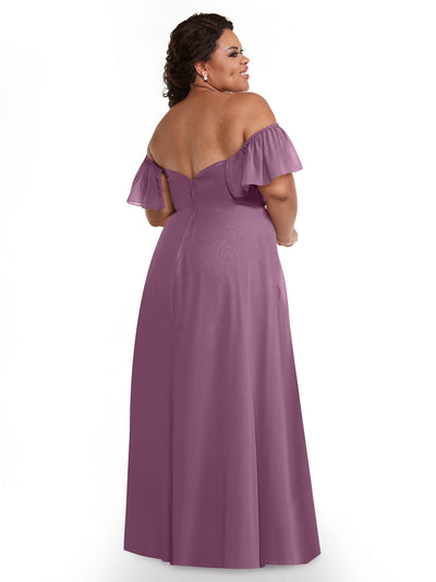 A woman in Avery Austin's mauve off-the-shoulder chiffon A-line gown (style 80168) stands facing away, smiling over her shoulder. The dress features ruffled sleeves and a fitted bodice.