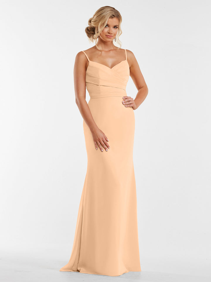 A woman stands against a plain white background wearing the Avery Austin 80169 blush chiffon dress, featuring a sleeveless design with thin straps and a fitted, pleated bodice.
