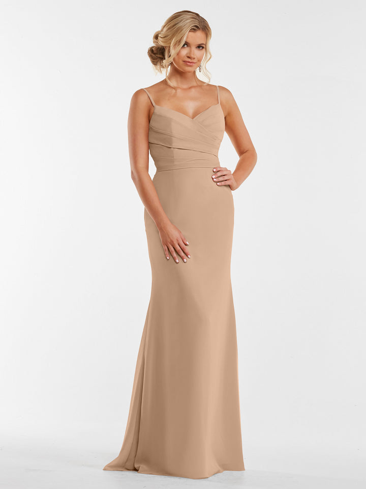 A woman poses with one hand on her hip, wearing the Avery Austin 80169—a buff floor-length fitted chiffon dress with thin straps and a pleated bodice—against a white background. Her hair is styled in a loose updo.