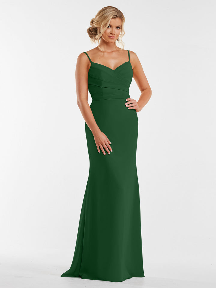A woman poses with one hand on her hip in Avery Austin style 80169, a sleeveless floor-length green chiffon dress with a pleated bodice. She stands against a plain white background, her blonde hair in an elegant updo.