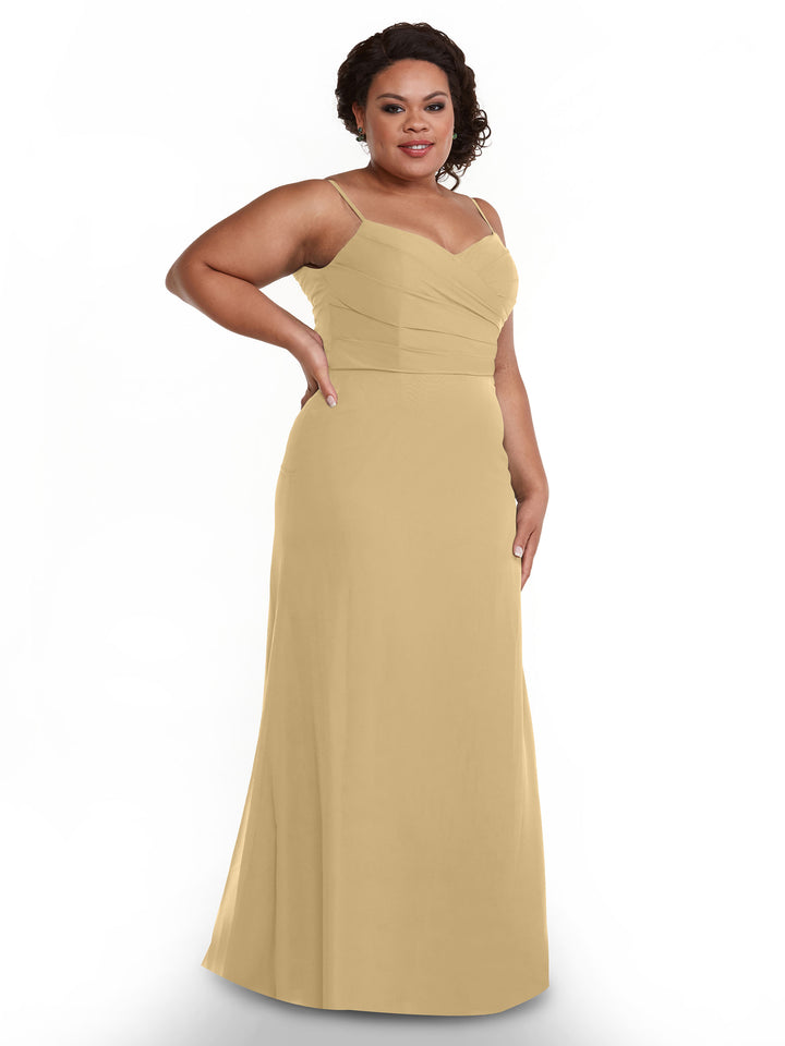A woman wearing Avery Austin’s floor-length, sleeveless champagne chiffon dress (style 80169) with spaghetti straps and a pleated bodice stands against a white background, smiling.