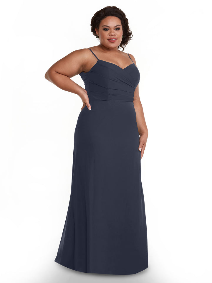 A woman poses in Avery Austin’s 80169: a sleeveless, floor-length navy chiffon dress with thin straps and pleated bodice. She stands against a white background, smiling with one hand on her hip.