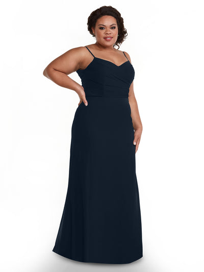 A woman models Avery Austin’s 80169, a sleeveless, floor-length navy chiffon dress with thin straps and a pleated bodice, posing confidently with one hand on her hip against a plain white background.