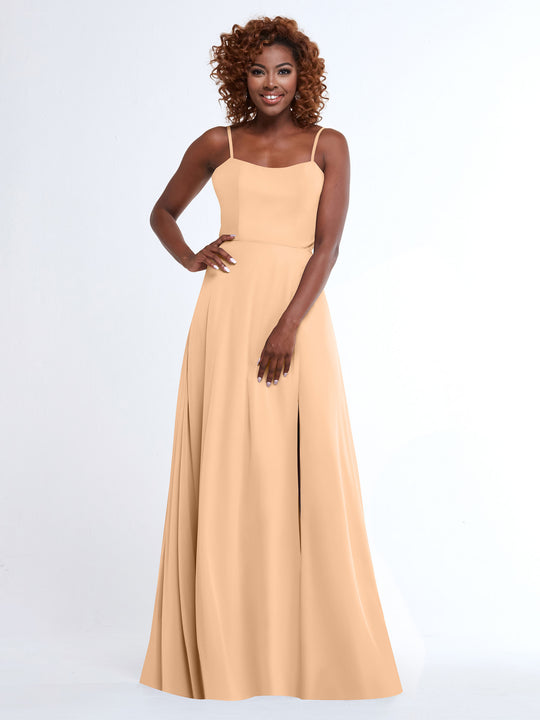 A smiling woman with curly hair poses against a plain white background, wearing the Avery Austin 80170: a light beige, sleeveless A-Line dress with spaghetti straps and a flowy design, her hand resting on her hip.