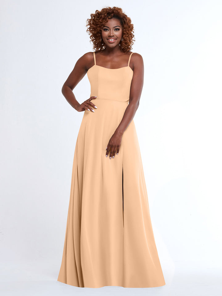 A smiling woman with curly hair poses against a plain white background, wearing the Avery Austin 80170: a light beige, sleeveless A-Line dress with spaghetti straps and a flowy design, her hand resting on her hip.