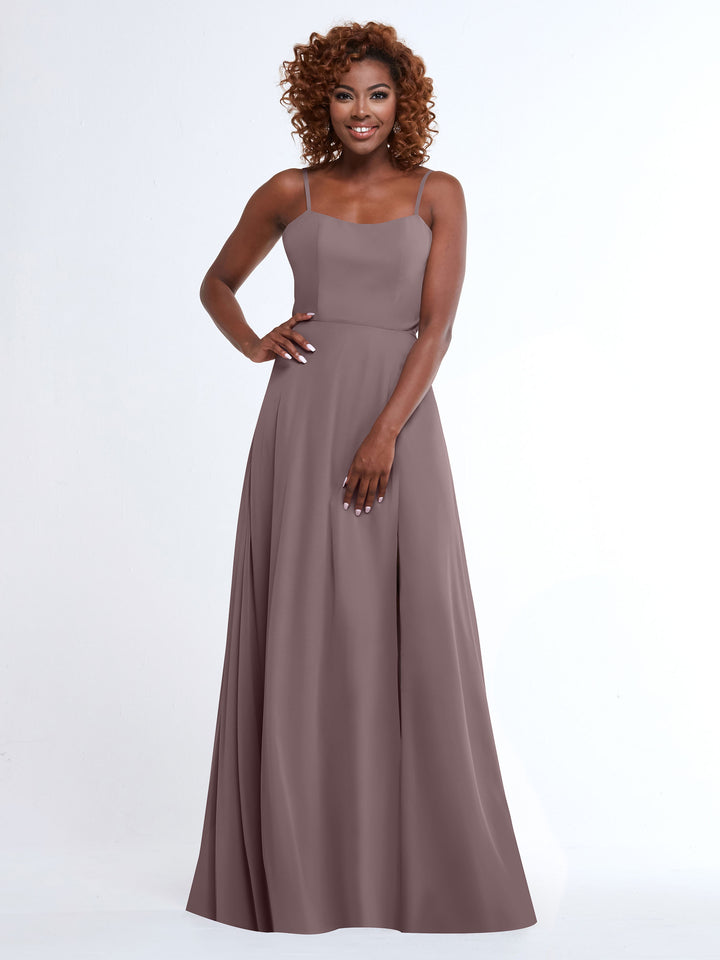 A woman with curly hair smiles while wearing the Avery Austin 80170, a flowy, floor-length mauve A-line dress with spaghetti straps, standing against a plain white background.