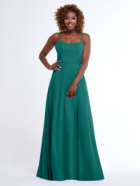 A woman with curly hair smiles in the Avery Austin 80170, a sleeveless, floor-length teal A-line dress with spaghetti straps, standing against a plain white background.