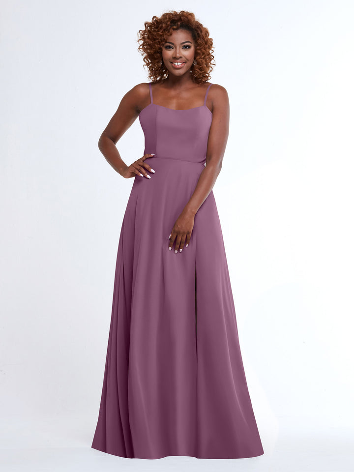 A woman with curly hair models the Avery Austin 80170, a flowy mauve A-Line dress with spaghetti straps, standing against a white background, smiling with one hand on her hip and the other on her skirt.