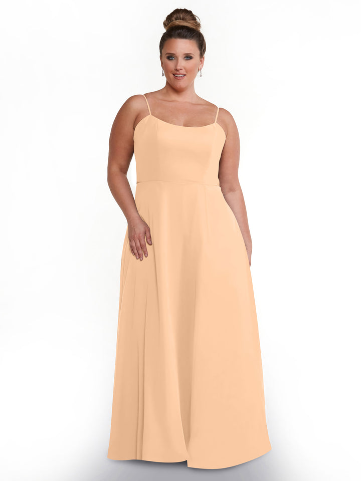 A woman with light brown hair in a bun models the Avery Austin 80170, a sleeveless peach A-line dress with spaghetti straps, standing against a plain white background.