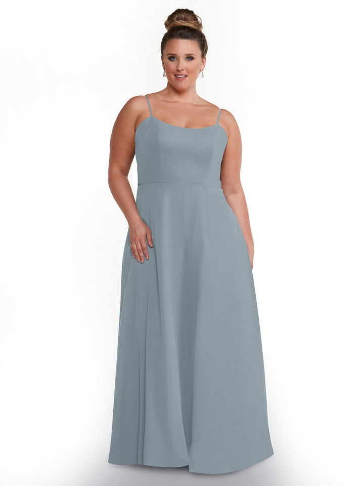 A woman with her hair in a bun is wearing the Avery Austin 80170 sleeveless, floor-length light gray-blue flowy dress with spaghetti straps and pockets, standing against a plain white background.