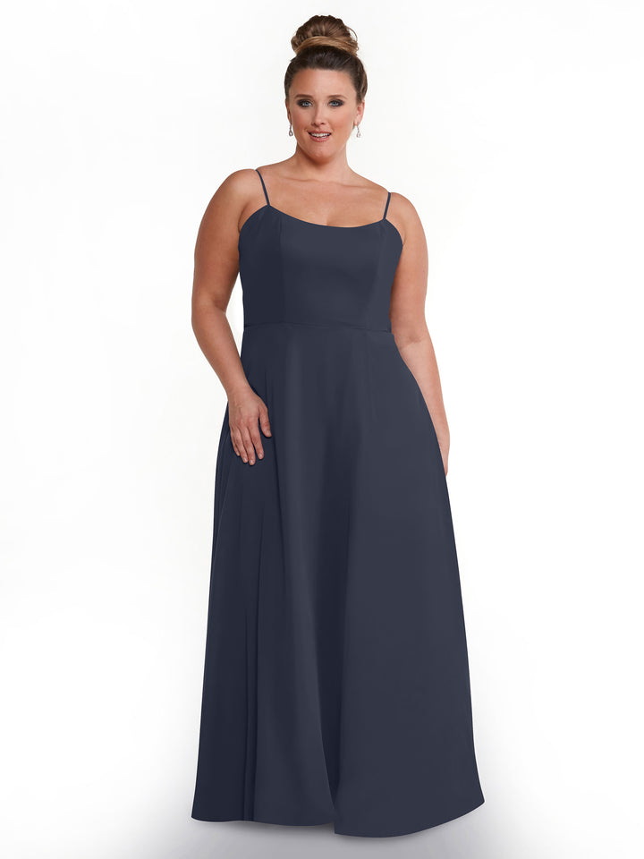 A woman with her hair in a bun models the Avery Austin TH-80170, a sleeveless navy blue A-Line dress with spaghetti straps and a fitted bodice, standing against a plain white background and smiling gently with one hand by her side.