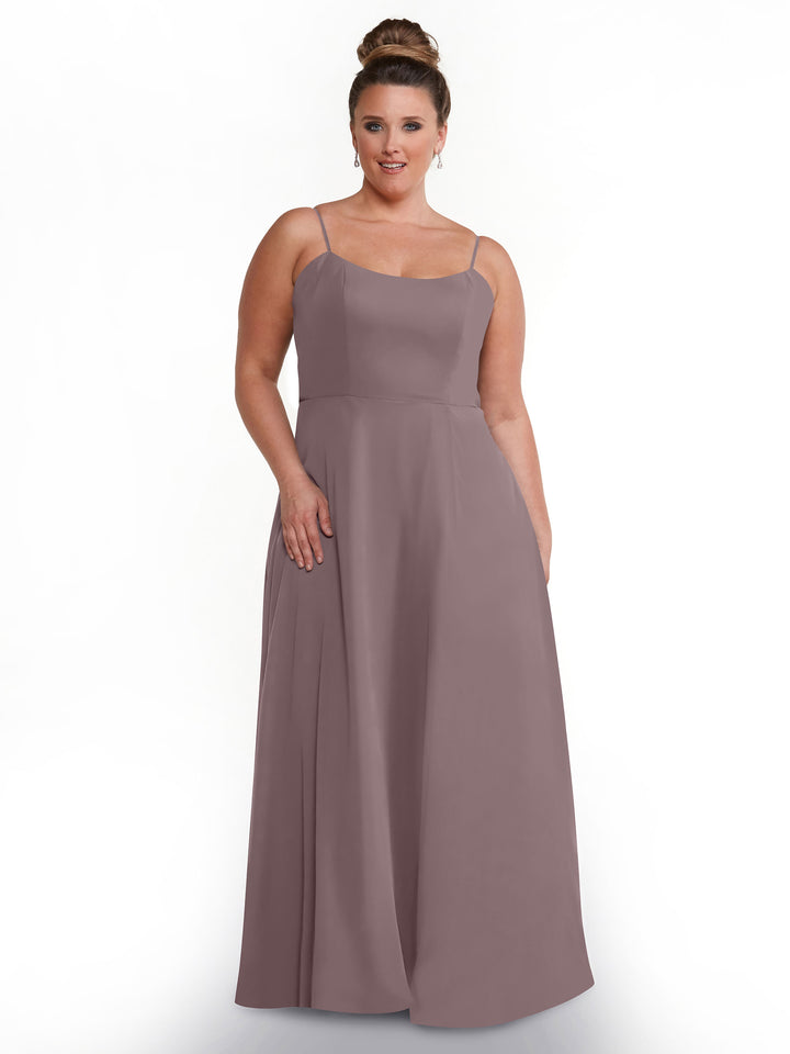 A woman with her hair in a bun wears Avery Austin’s 80170, a mauve, flowy A-line dress with spaghetti straps and side pockets, standing against a plain white background.