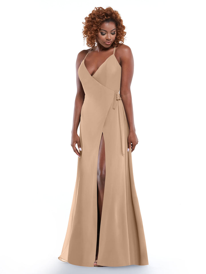 A woman with curly hair models Avery Austin’s 80171—a sleeveless beige floor-length wrap dress featuring a deep V-neckline, self-tie sash, and slit—standing against a plain white background.