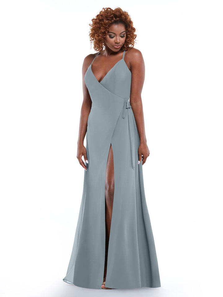 A woman with curly hair stands against a white background wearing Avery Austin style 80171, a light gray sheath dress with a V-neck, wrap bodice, self-tie sash, and high leg slit.