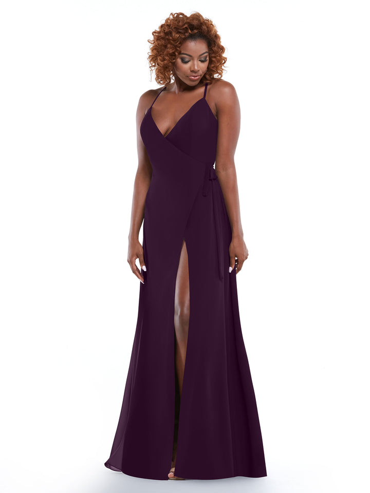A woman with curly hair models the Avery Austin 80171 deep purple dress, featuring spaghetti straps, a V-neckline, and a high front slit, standing against a plain white background.