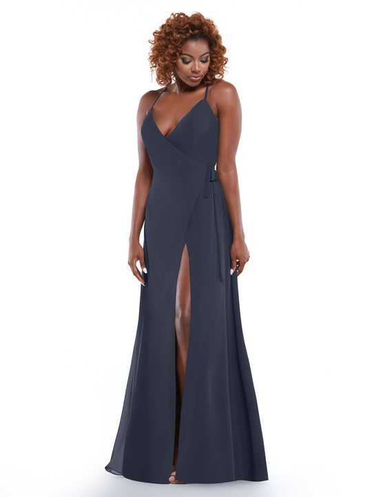 A woman with curly hair models Avery Austin's TH-80171 dress in indigo—a sleeveless, floor-length sheath with a V-neckline, thin straps, high slit, and self-tie sash—against a plain white background.