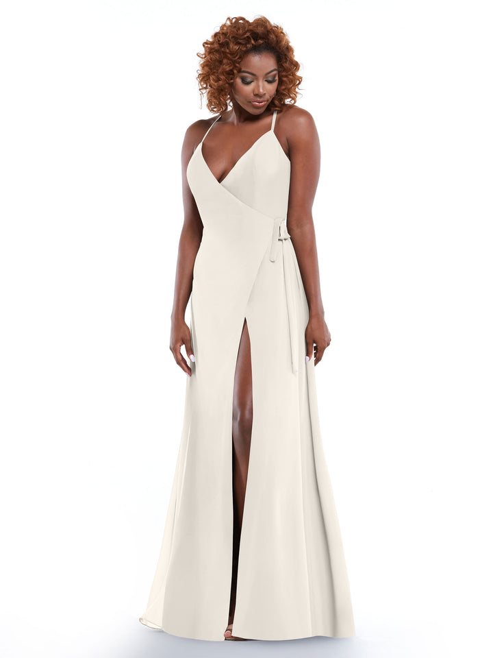 A woman wears the Avery Austin 80171, a sleeveless ivory sheath dress with a wrap-style bodice, self-tie sash, and high front slit. She stands against a white background and gazes downward with a slight smile.