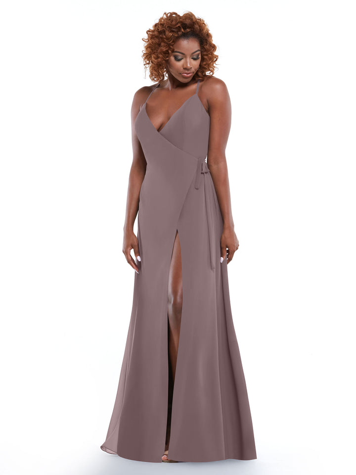 A woman with curly hair wears Avery Austin’s 80171, a mauve sleeveless wrap dress with a deep V-neckline, thigh-high slit, and self-tie sash, standing against a plain white background.