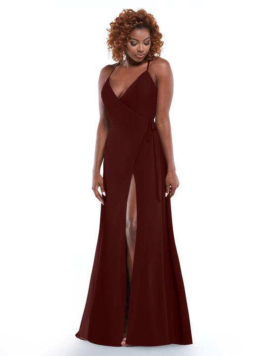 A woman with curly hair models Avery Austin's 80171 deep red slit dress with a self-tie sash, standing against a plain white background and smiling slightly while looking down.