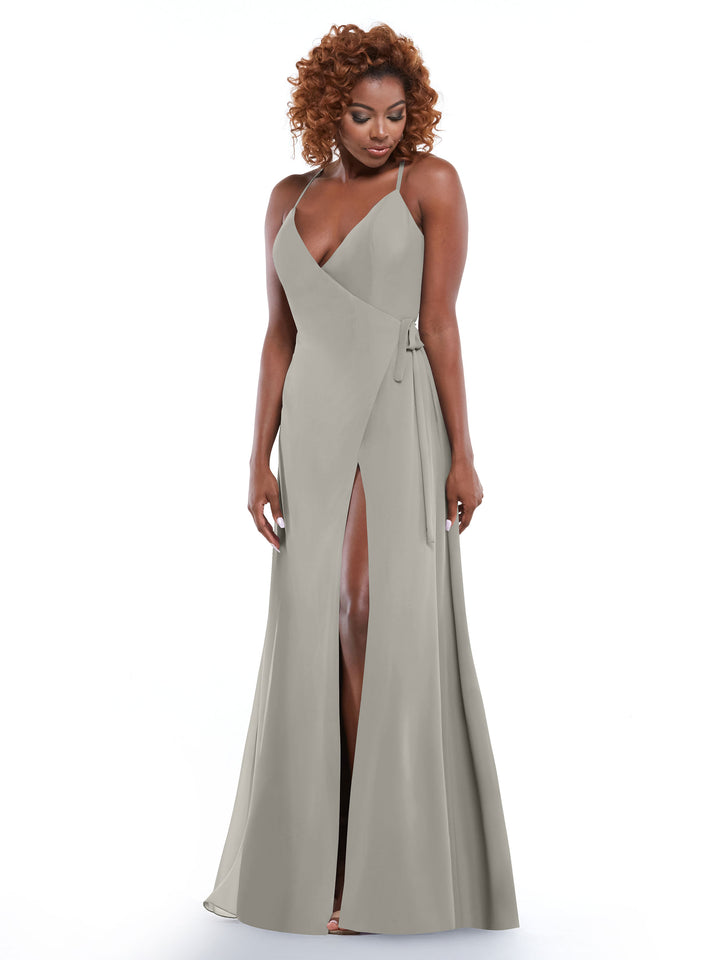 A woman with curly hair models Avery Austin’s 80171: a sleeveless, floor-length light gray dress with a V-neckline, high front slit, and self-tie sash, standing against a plain white background.