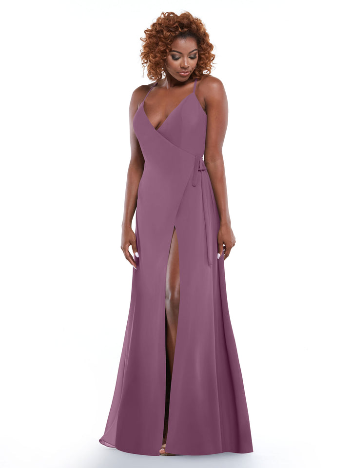 A woman with curly hair models Avery Austin’s 80171, a sleeveless mauve dress featuring a deep V-neckline, self-tie waist sash, and high front slit, posed against a plain white background.