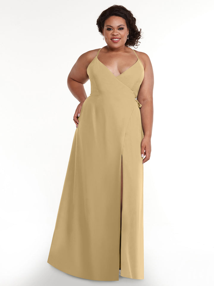 A woman smiles with one hand on her hip, modeling the Avery Austin 80171—a sleeveless tan slit dress with a V-neckline and self-tie sash—against a plain white background.