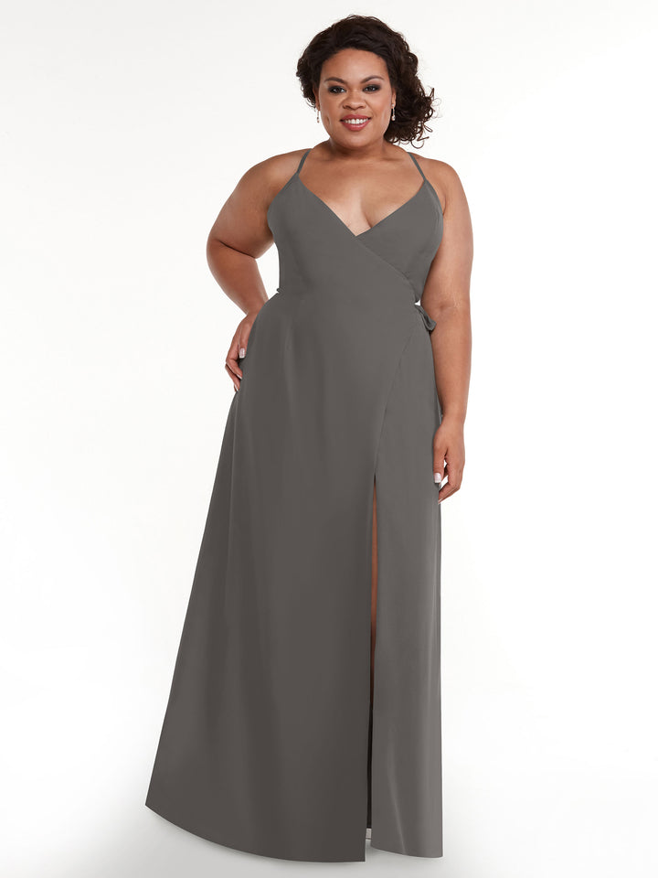 A woman smiles against a white background wearing the Avery Austin TH-80171, a sleeveless steel gray floor-length sheath dress featuring a V-neckline, high slit, and self-tie sash.