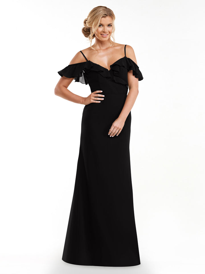 A woman smiles with one hand on her hip, modeling the Avery Austin 80172—a long black A-line dress featuring a ruffled neckline and off-the-shoulder sleeves—against a plain white background.