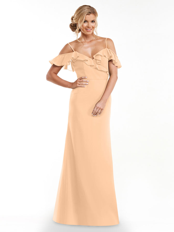 A woman smiles against a white background, modeling Avery Austin’s 80172: a long, peach A-line dress with off-the-shoulder sleeves and a ruffled neckline.