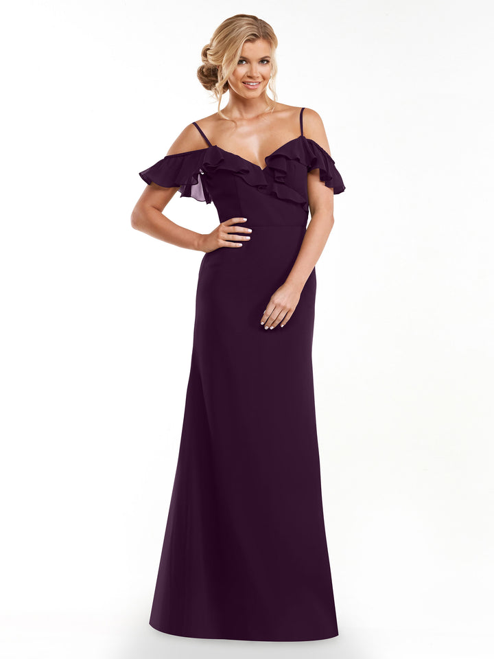 A woman in the Avery Austin 80172, a floor-length dark purple A-line dress with spaghetti straps and ruffled off-the-shoulder sleeves, stands smiling against a plain white background with one hand on her hip.