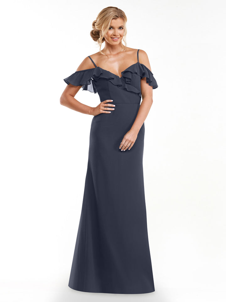 A woman models Avery Austin’s floor-length A-line dress (Style 80172) in dark blue, featuring thin straps and ruffled off-the-shoulder sleeves, smiling with one hand on her hip against a white background.