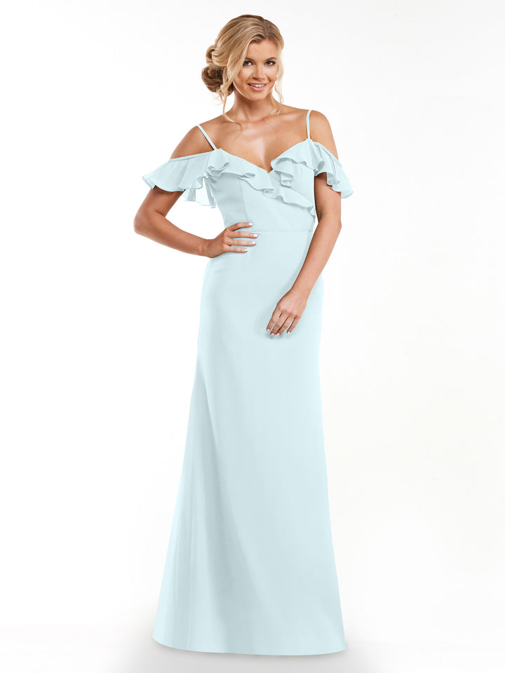 A woman stands smiling against a white background wearing Avery Austin’s 80172, a light blue, floor-length A-line dress with off-the-shoulder sleeves and ruffle details.