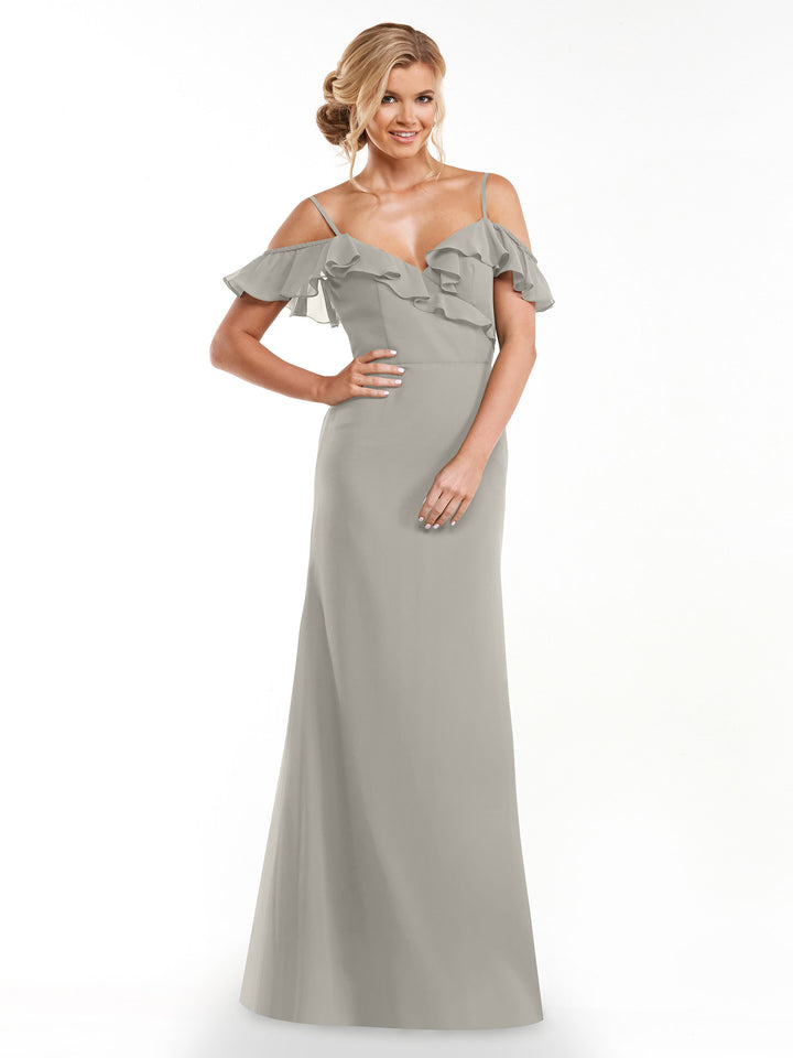 A woman smiles against a white background, wearing Avery Austin’s 80172: a light gray, floor-length A-line dress with a ruffled neckline and off-the-shoulder sleeves.