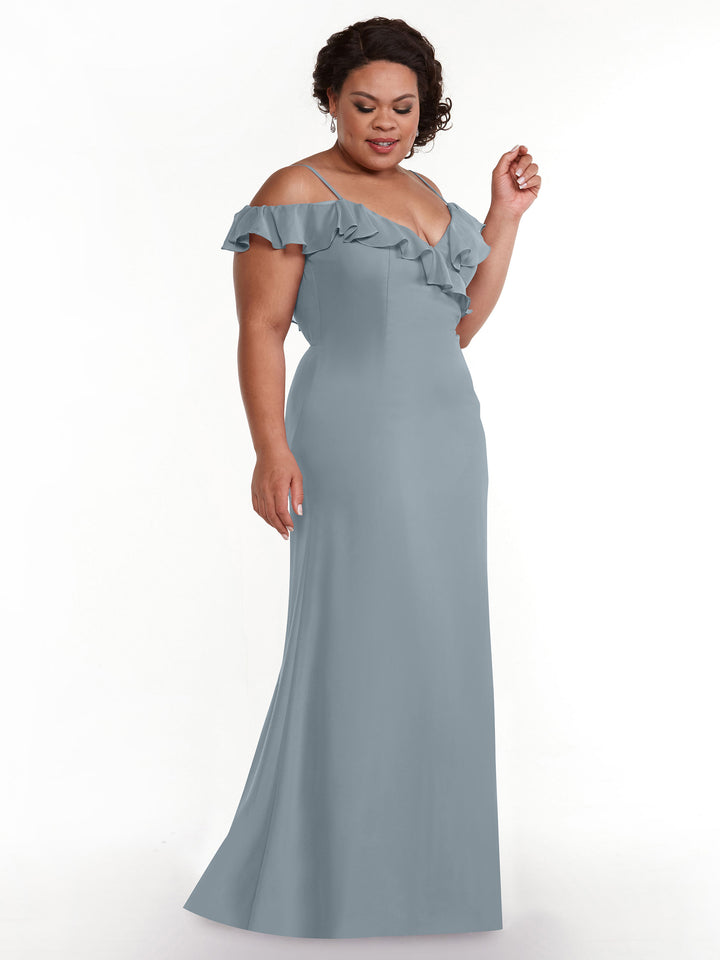 A woman models Avery Austin’s 80172: a light blue A-line dress with off-the-shoulder sleeves and a ruffled neckline. Against a white background, she looks down with a slight smile and her curly hair styled up.