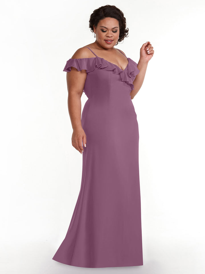 A woman poses against a white background, wearing Avery Austin’s TH-80172—a Wisteria A-line gown with off-the-shoulder sleeves and a cascading ruffled neckline that flows into the floor-length skirt.