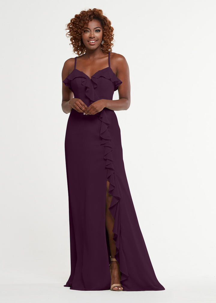 Model wears Avery Austin 80174: a sleeveless deep purple A-line dress with ruffle detailing and a thigh-high slit, standing against a white background and smiling with her curly hair.