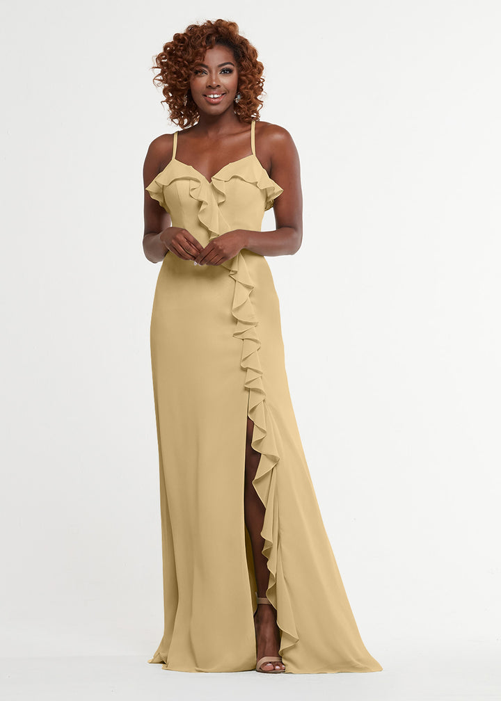 A woman wearing Avery Austin’s 80174, a long light gold A-line dress with spaghetti straps, a sweetheart bodice, and thigh-high slit, stands against a white background, smiling with her hands gently touching in front.
