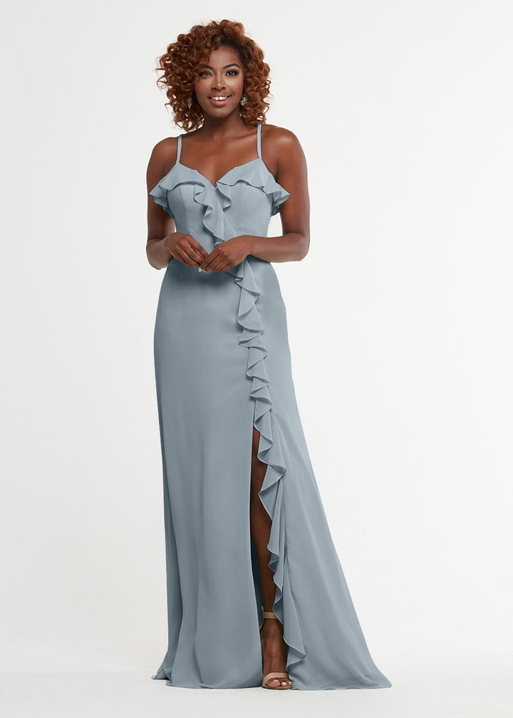 A woman smiles in Avery Austin’s 80174: a light blue, floor-length ruffled dress with thin straps, sweetheart bodice, and thigh-high front slit, standing against a plain white background.