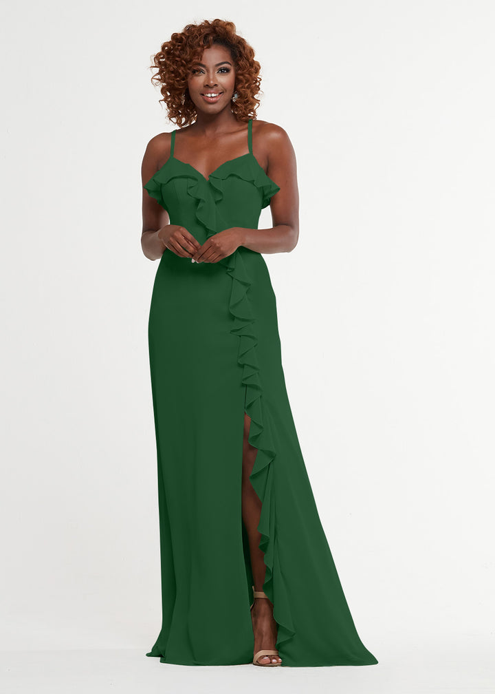 A woman with curly hair smiles while wearing Avery Austin’s 80174: a ruffled, sleeveless sweetheart emerald green A-line gown with a thigh-high slit, standing against a plain white background.