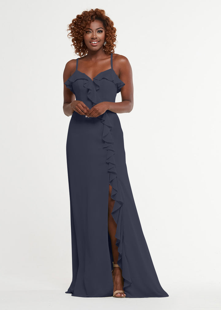 A woman with curly hair models Avery Austin style 80174—a navy, floor-length ruffled dress with thin straps, a sweetheart bodice, and a side slit—against a plain white background.